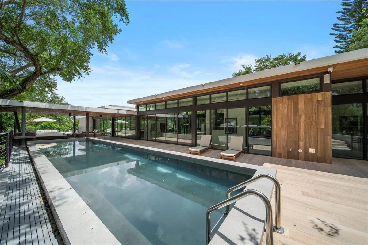 Brickell Avenue spec home: long glass pavilion with floor-to-ceiling sliders along the pool deck under mature oaks
