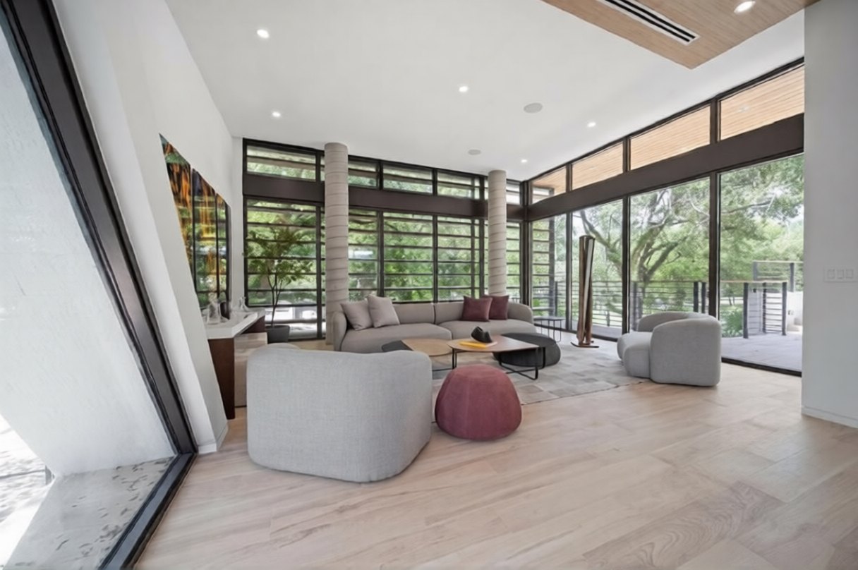 Upstairs living room walled in floor-to-ceiling glass under clerestory windows, opening to a balcony in the oaks