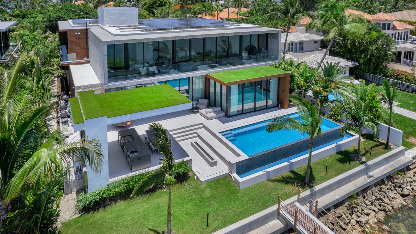 Aerial of the Hibiscus Island spec home: glass volumes, green roofs and pool on the bay