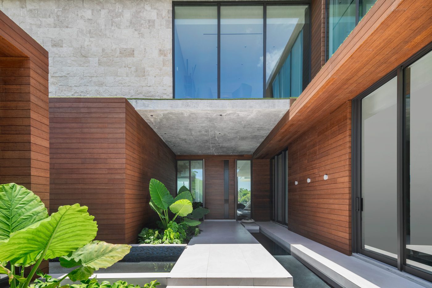 Entry court framed by wood-clad walls and full-height glazing