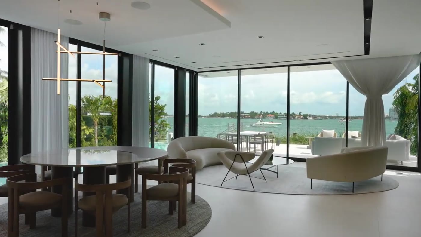 Living and dining room walled in floor-to-ceiling glass on the bay
