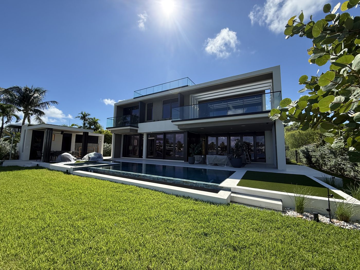 North Shore custom home on the water: glass-railed balconies and roof deck above a wall of folding doors and the pool
