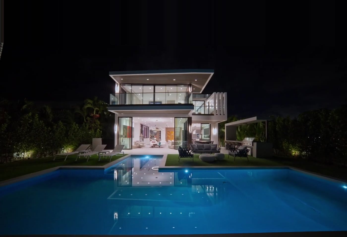 Normandy Shores custom home at night: two stories of glass lit above the pool on the bay