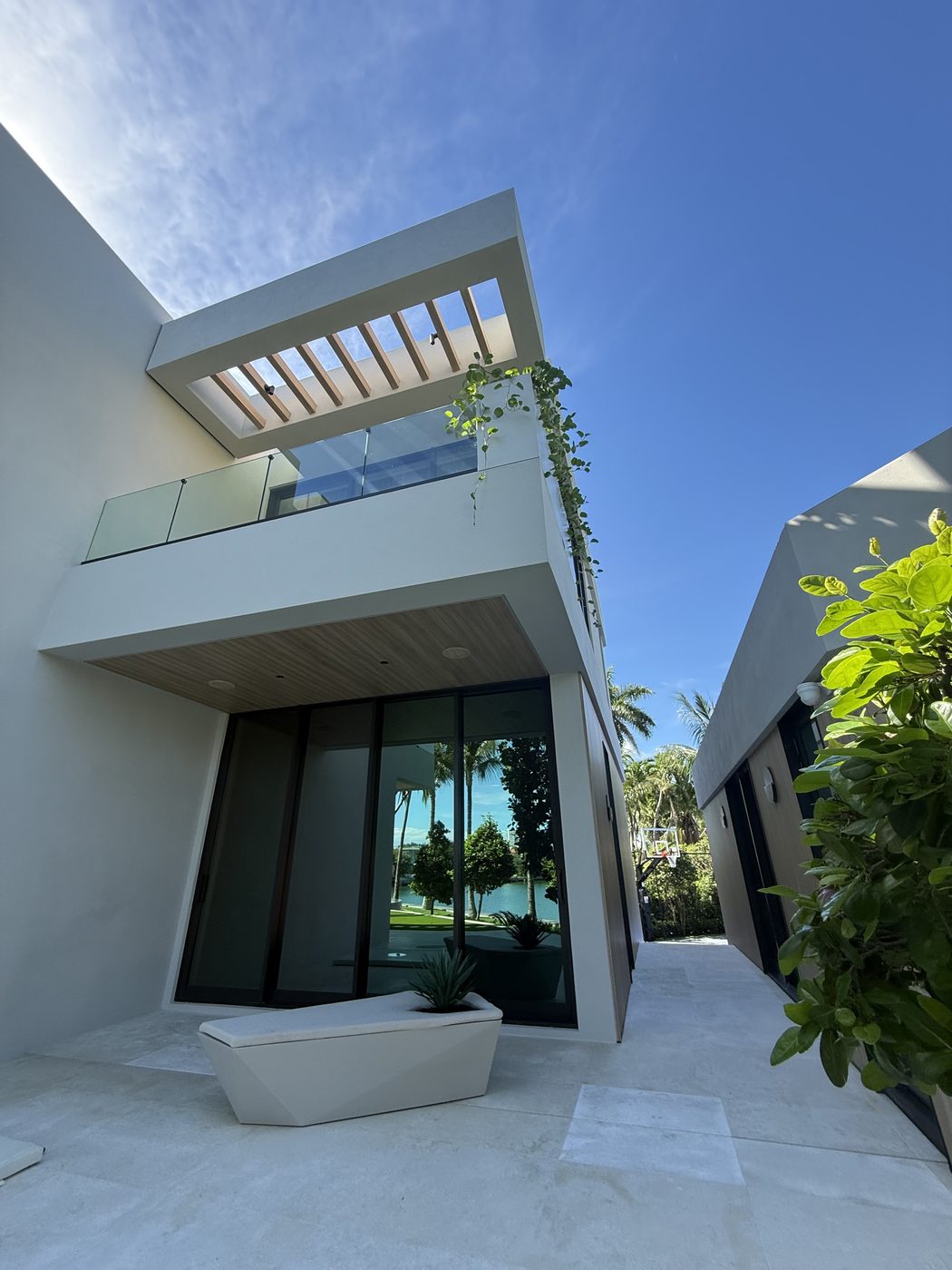 Frameless glass balcony railing under a wood-slat trellis
