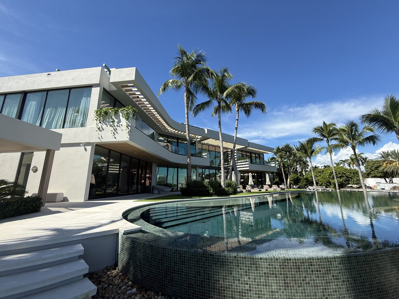 Infinity pool curving along the rear of the house beneath the glass-railed terrace