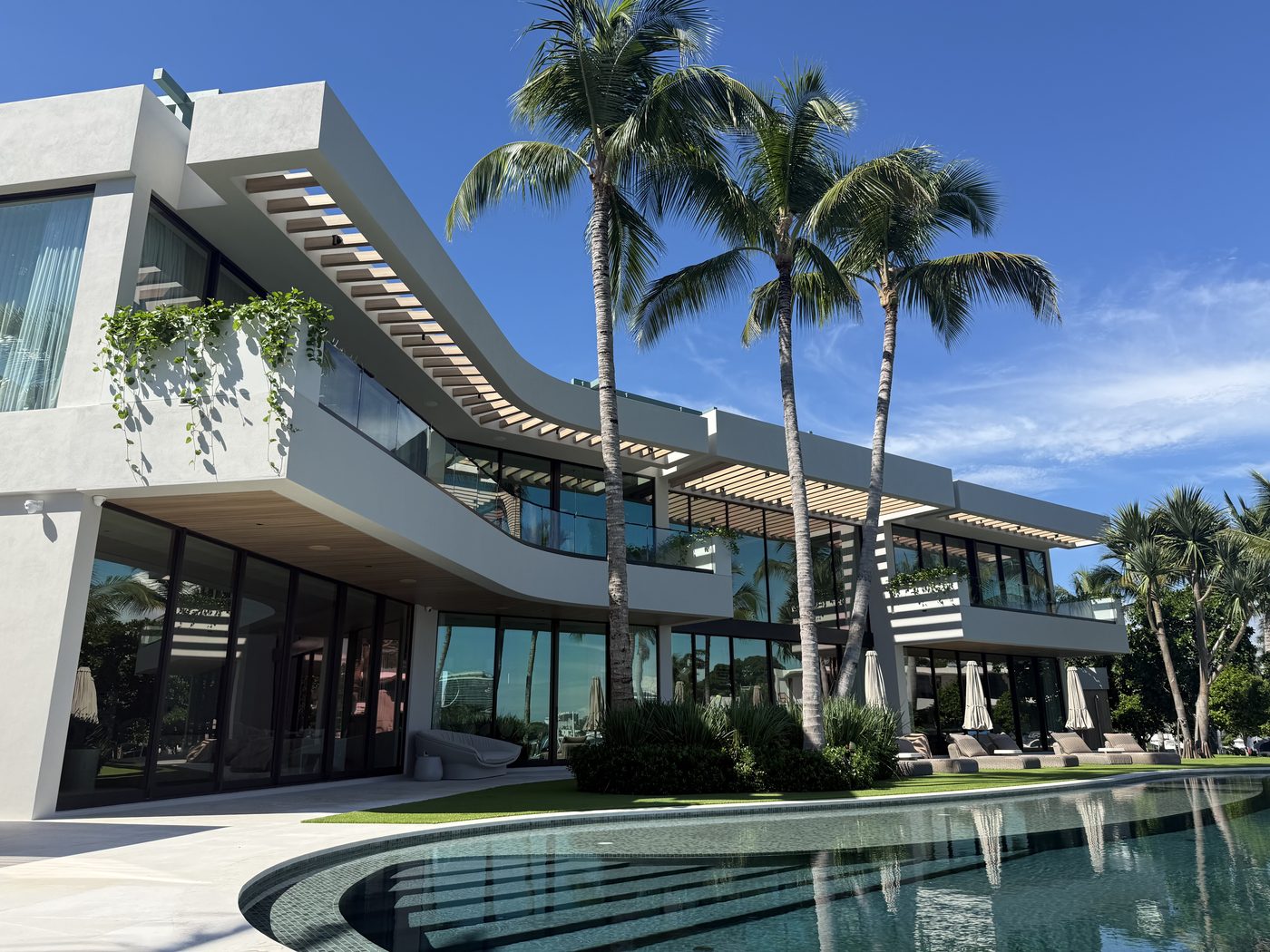 Pinetree Drive custom home: curved upper terrace with frameless glass railing over the pool and Indian Creek