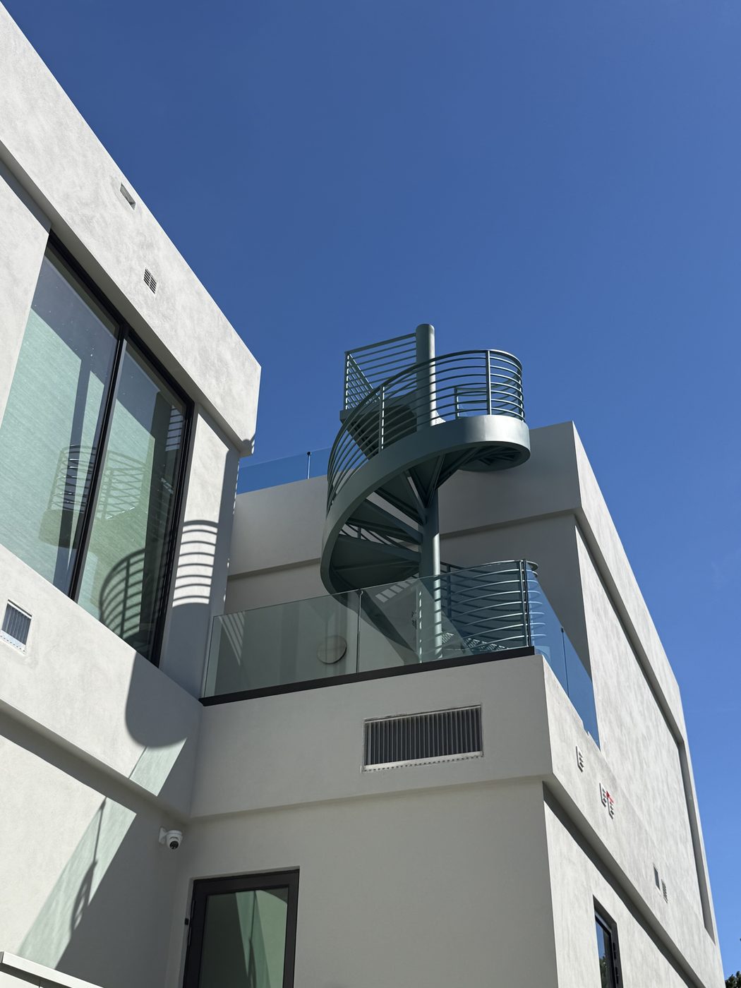 Spiral stair to the roof deck above a frameless glass terrace railing