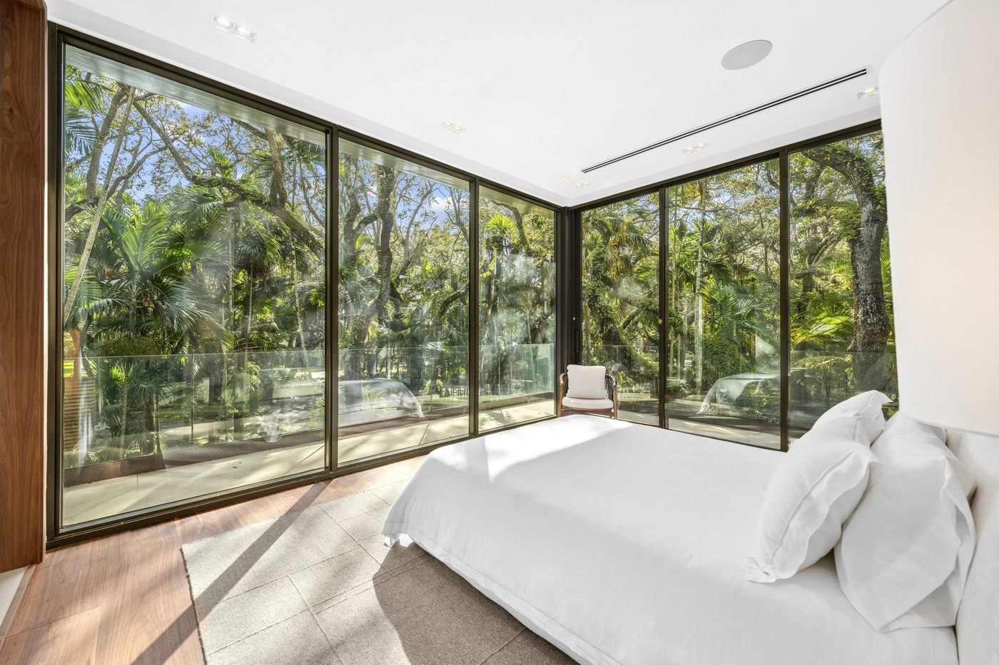 Corner bedroom wrapped in floor-to-ceiling sliding glass with a glass balcony railing