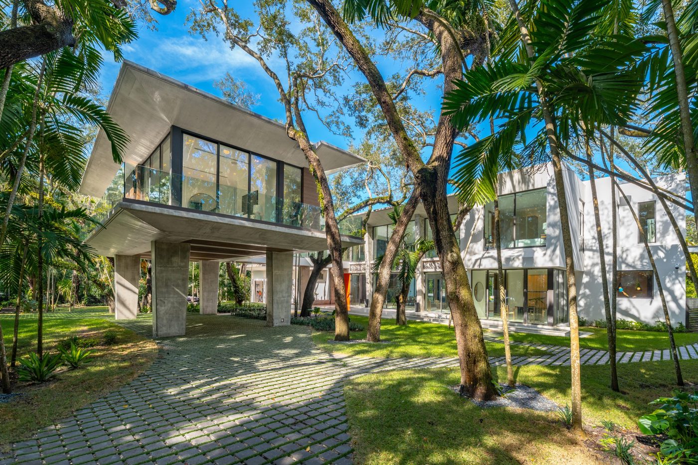 Snapper Creek spec home: glass pavilion raised on concrete piers among live oaks, with frameless glass railings